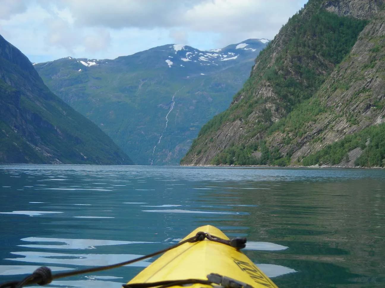 Étrave jaune d'un kayak sur le Geirangerfjord, face aux parois et à une cascade