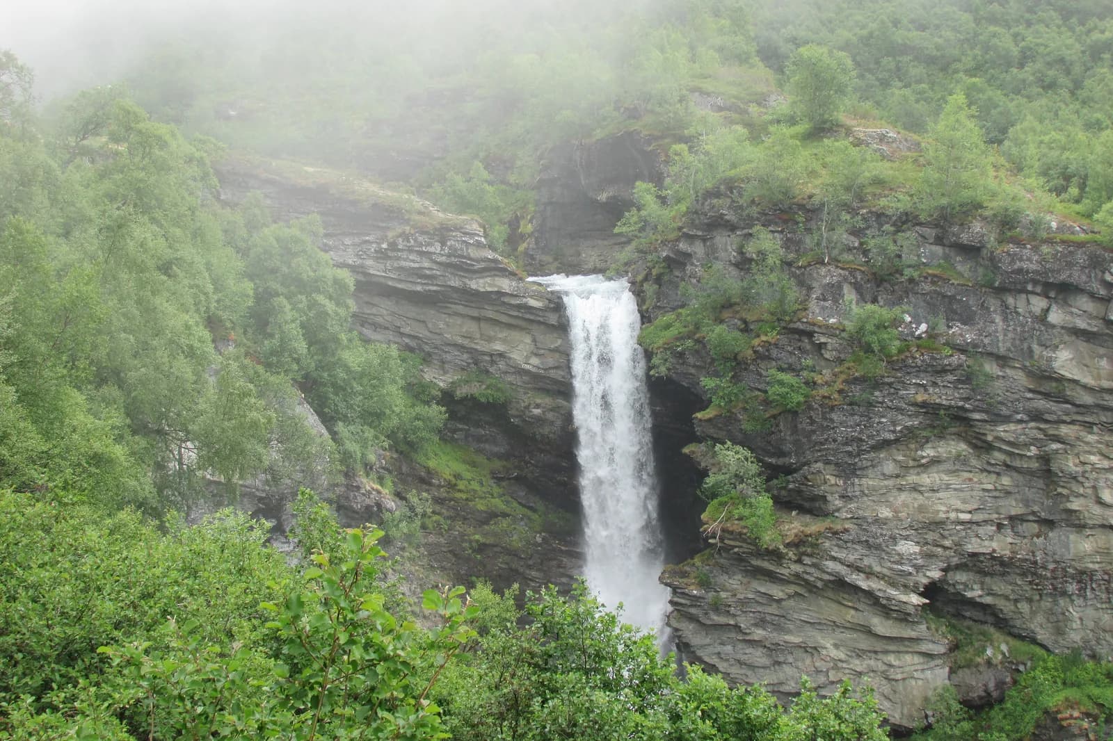 La cascade de Storsæterfossen jaillissant d'une paroi rocheuse dans la brume, au-dessus de Geiranger