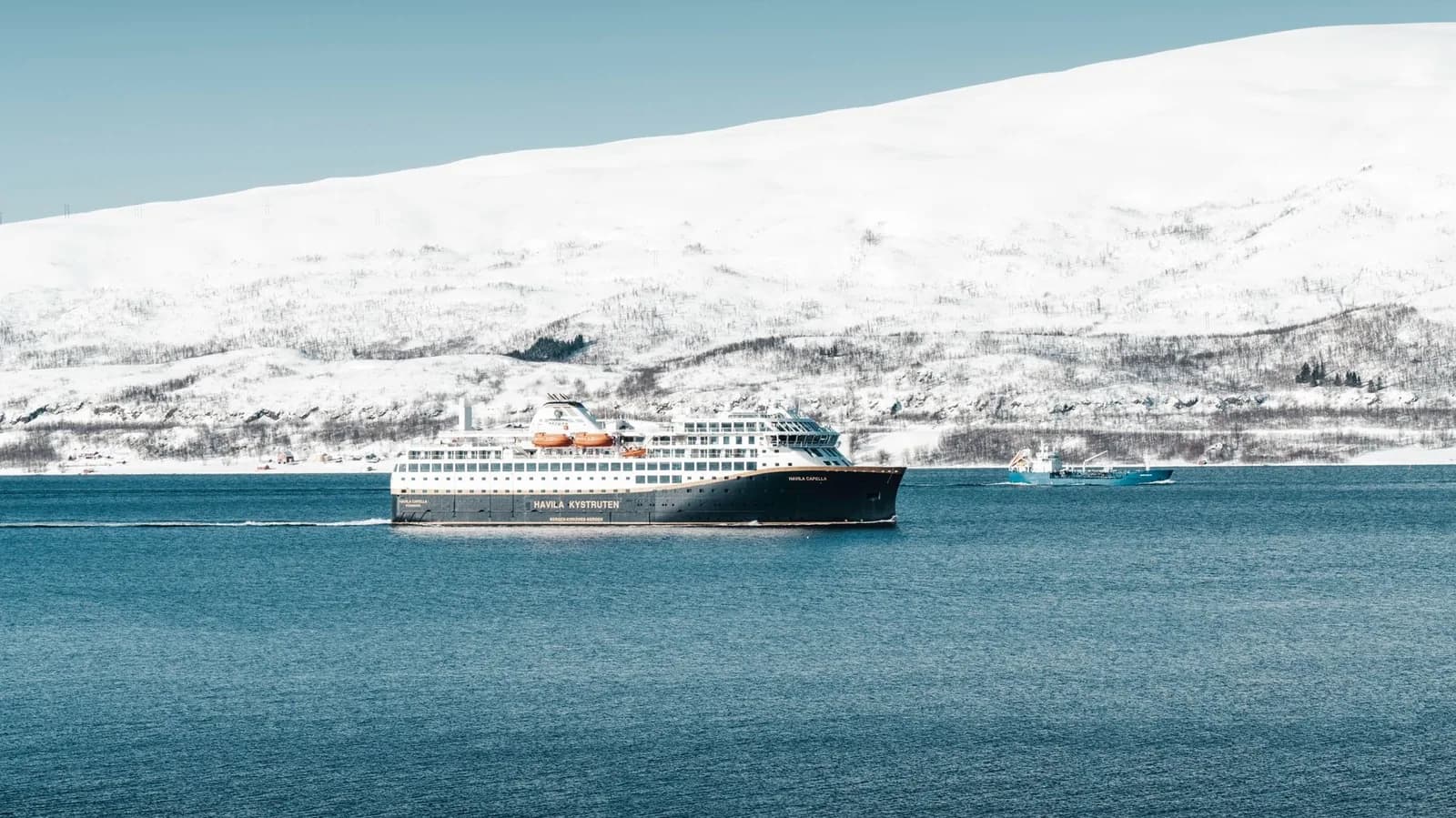 Le navire Havila Capella de l’express côtier dans un fjord, devant une montagne couverte de neige