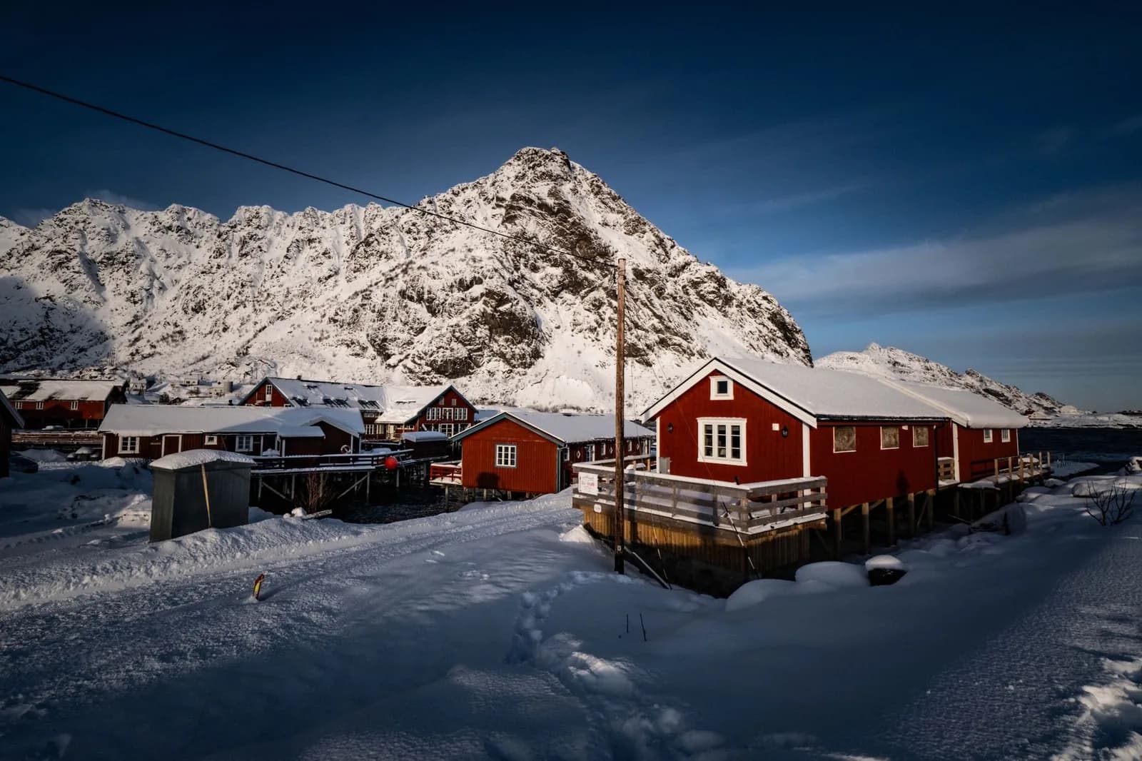 Cabanes rouges de pêcheurs (rorbuer) enneigées au pied d’une montagne, aux îles Lofoten