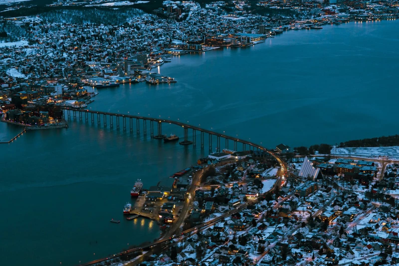 Vue aérienne de Tromsø enneigée dans la lumière bleue du crépuscule de la nuit polaire, avec le pont de Tromsø au-dessus du détroit