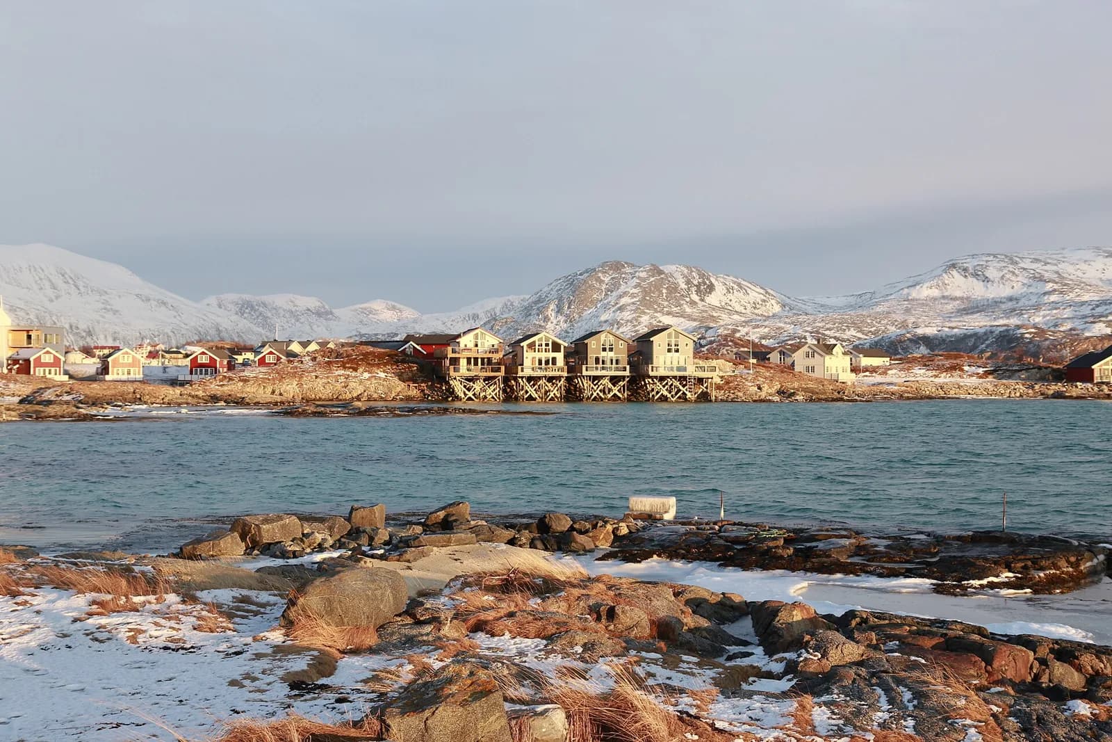 Maisons sur pilotis au bord de l’eau à Sommarøy, près de Tromsø, avec des montagnes enneigées